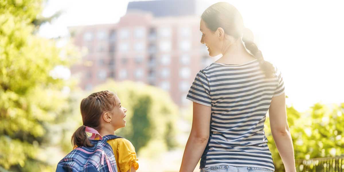 Mom walking daughter to the bus stop to go back to school